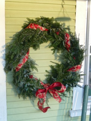 a hemlock wreath with red ribbon hanging by our front door