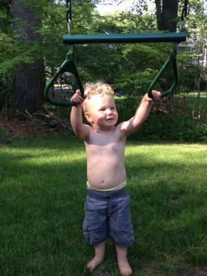 Lijah holding on to the rings/bar on a neighbor's play structure (feet firmly on the ground)