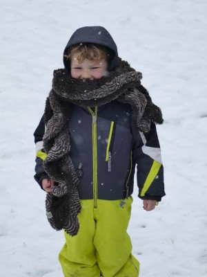 Lijah in the snow in his snowsuit, wearing a big scarf