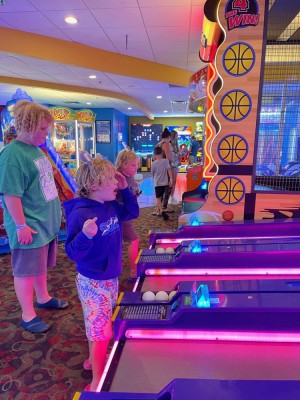 the boys at a skiball machine in a brightly colored arcade