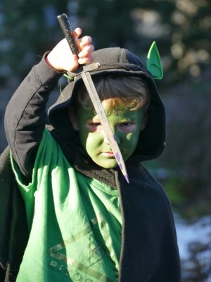 Lijah with green face paint, goblin ears, black cloak, and knife