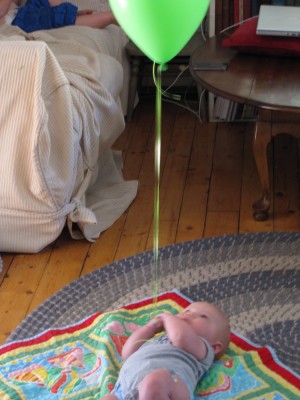 Elijah, on the ground, holding onto the string of a green helium balloon