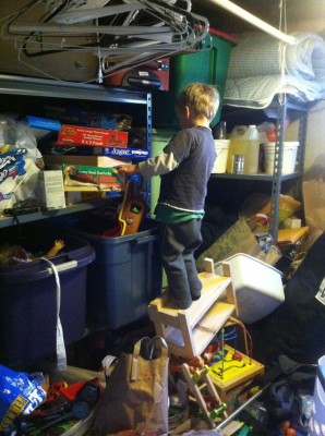Zion standing on a precarious pile of junk, reaching for a toy in the messy basement