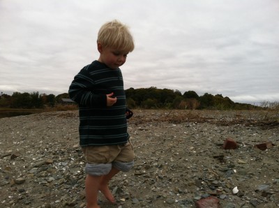Zion, barefoot with rolled-up pants, walking on the gravel beach