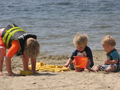 the three boys digging in the sand with water behind them