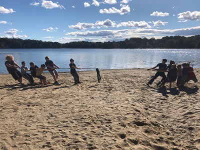 the boys and a bunch of other kids playing tug of war on a pond beach