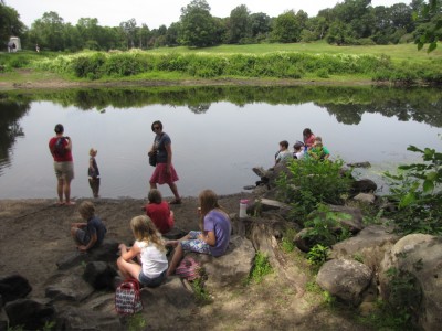 lots of kids picnicing on the shores of the Concord River