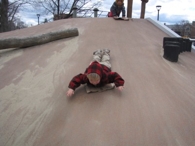 Zion sliding down a sandy concrete slope head first on a piece of cardboard