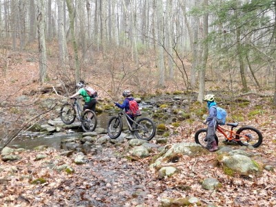 the boys pushing their bikes across a wide rocky stream
