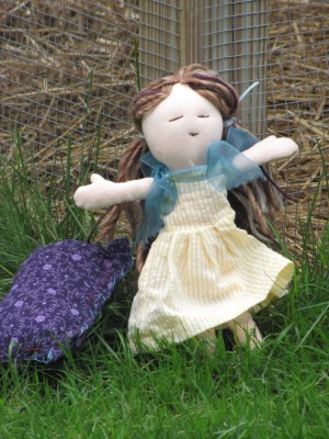 a doll with brown hair and a yellow dress, with her purple pillow