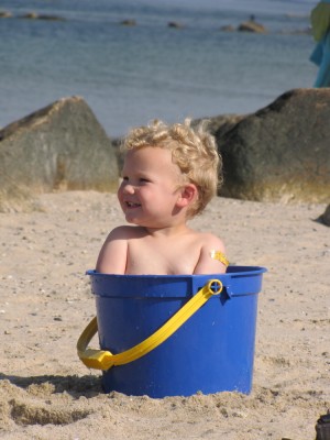 Lijah sitting in a big blue bucket on the beach