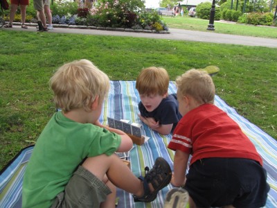 Zion and Nathan playing cards on a picnic blanket, Lijah looking on