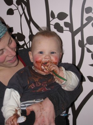 Lijah with chocolate pudding all over his face and clothes, held by Mama