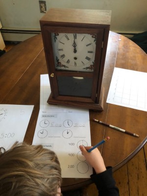 Elijah in front of a clock doing a worksheet