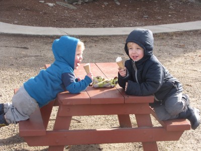 Zion and Lijah, hooded, eating ice cream cones at a little picnic table