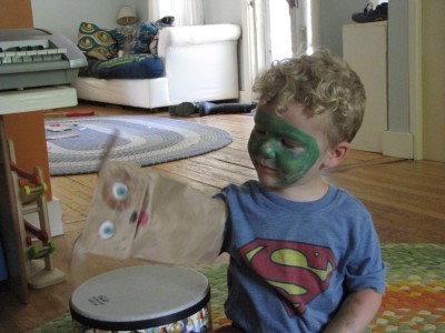 Lijah in green facepaint playing with a paper-bag puppet