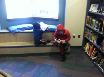 Harvey and Zion reading books in the library in their winter coats
