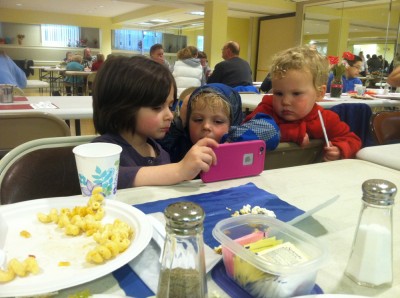 Zion and Lijah watching a show on a friend's phone at the community dinner