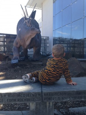 Lijah in tiger pajamas lounging on a wall in front of a statue dinosoar