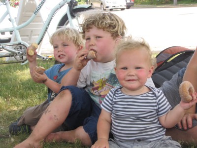 Zion, Harvey, and Lijah sitting on the grass eating doughnuts