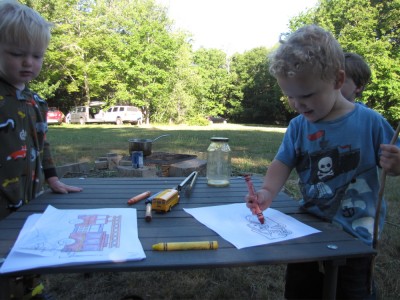 Lijah and Henry working on coloring pages by the remains of the fire