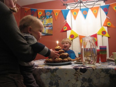 Elijah looking at a birthday candle on a pile of muffins, Zion singing in the background