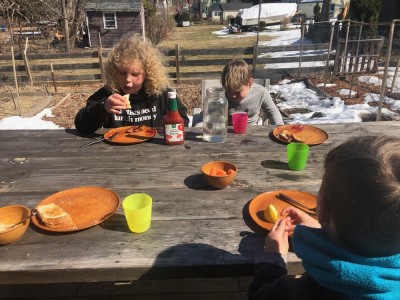 the boys eating lunch at the picnic table with snow in the background