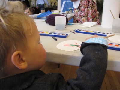 Lijah reaching up high to paint a paper egg on a table