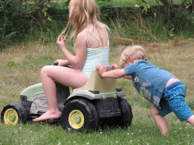 Zion pushing Megan on the pedal tractor