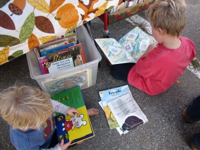 Zion and Harvey sitting on the pavement in the book sale booth looking at books