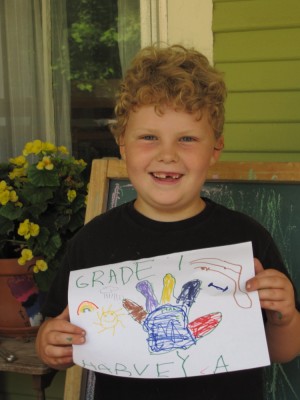Harvey on the front porch, smiling and holding his Grade 1 sign