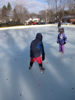 Harvey drooping on his skates on the outdoor rink, Nisia watching