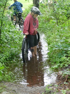 Harvey standing with his bike ankle-deep in water on a path