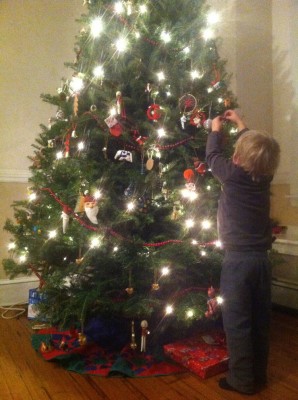 Zion reaching up to put an ornament on a Christmas tree