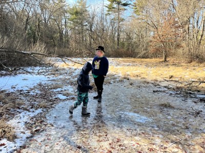 Harvey and Elijah sliding on a big frozen puddle in a clearing