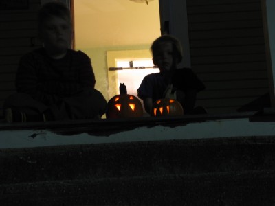 Zion and Harvey sitting on the dark porch with their jack-o-lanterns