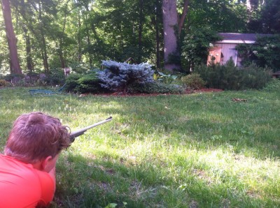 Harvey lying on the ground shooting the BB gun at a target