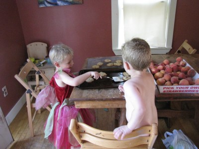 Zion in a dress taking cookies off the sheet, naked Lijah watching