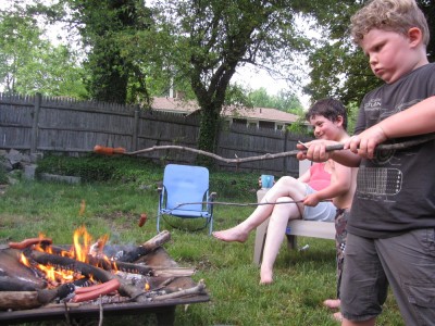 Harvey looking serious holding a hot dog on a stick over a fire