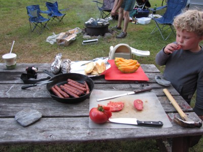 the picnic table with a skillet of hot dogs and a cut-up tomato. and Harvey