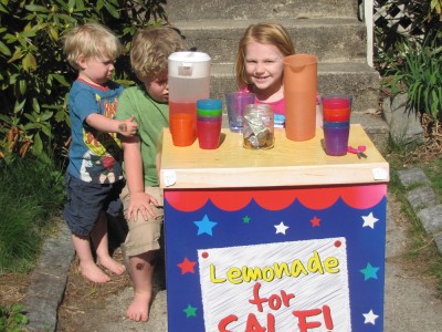 Harvey and Zion (both looking grumpy) with a friend and their lemonade stand