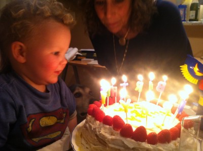 Lijah looking at a birthday cake glowing with the light of candles spelling out 