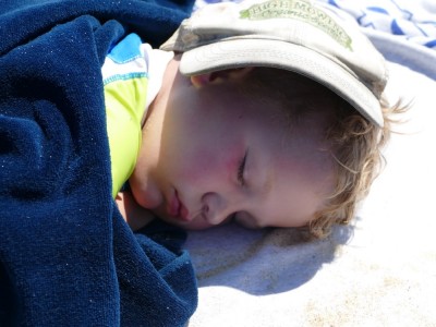 Lijah sleeping on the beach with my cap over his face