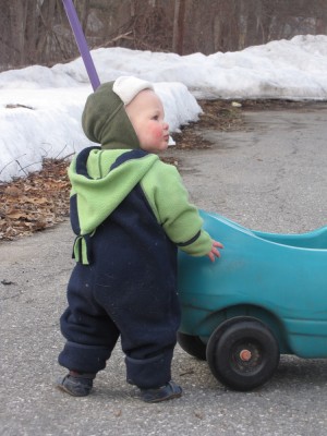 Lijah in his snowsuit walking in the road holding on to a push car