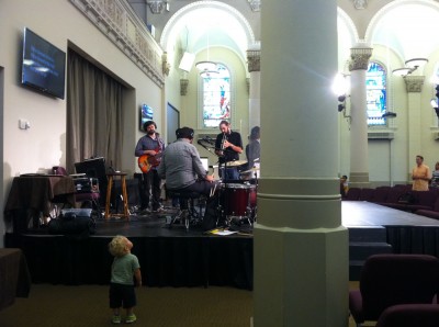 Lijah standing next to the stage at church during worship; the bass player is looking at him