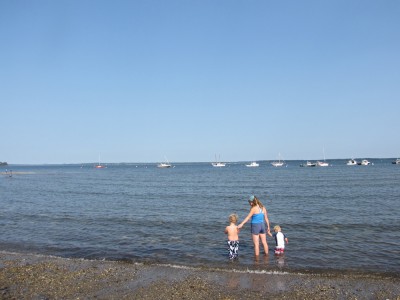 Leah and the boys wading in the ocean with boats moored in the background