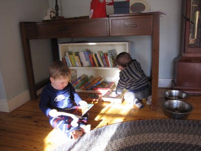 Lijah sitting on the living room floor reading a book, baby Joan Marc behind him