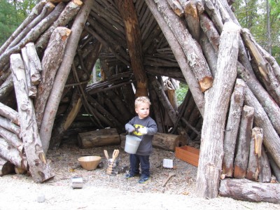 Lijah standing in a log wigwam-like structure