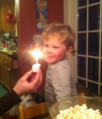 Lijah smiling at a candle burning in a marshmallow held before him
