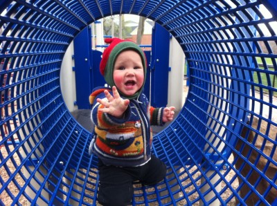 Lijah in the cage tube at the playground, reaching for the camera